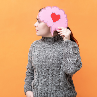 Woman holding a brain-shaped paper with a heart on it next to her head.